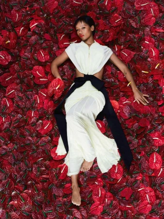 Overhead shot of a woman in a white dress with a black sash lying on a bed of red anthurium flowers in a fashion editorial.