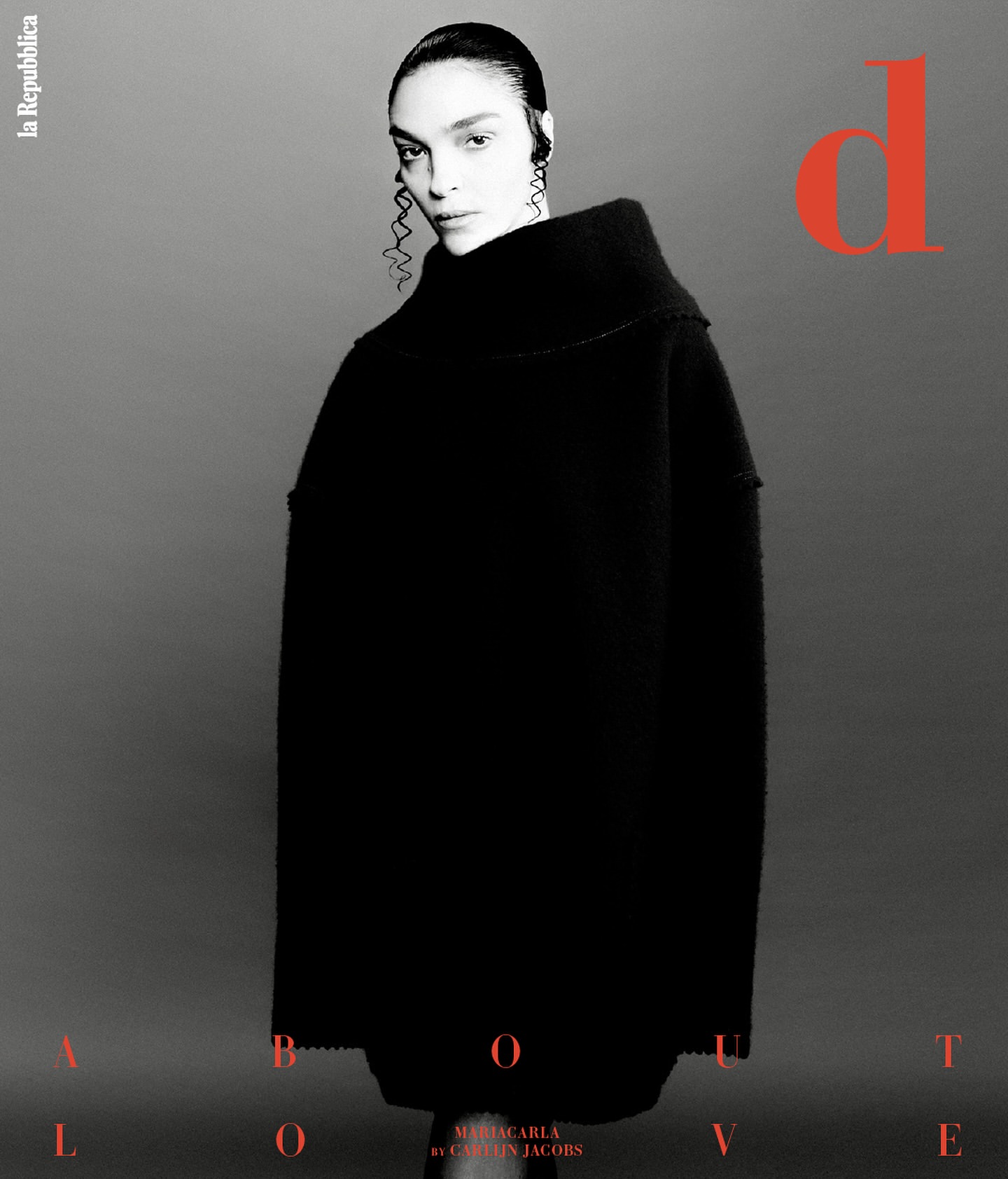 Black and white fashion shot of a woman wearing a black turtleneck sweater with statement earrings against a gray background.