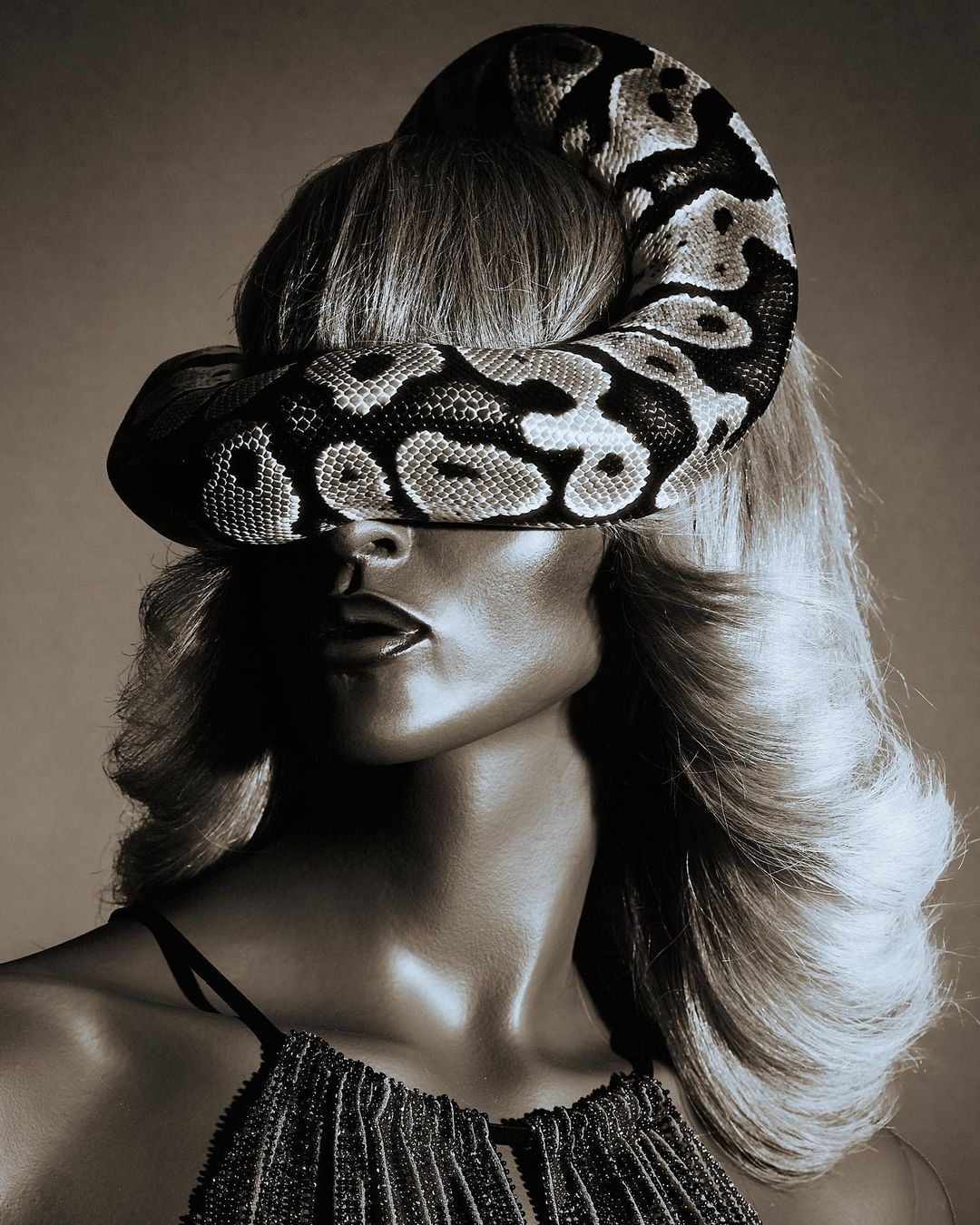 Surreal portrait of a woman with blond wavy hair wearing a snake like a hat against a neutral background, beauty and fashion concept.