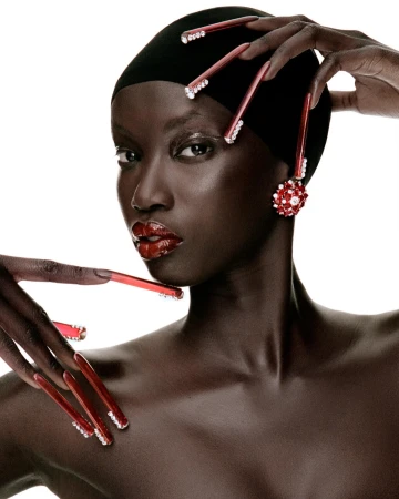 Close-up shot of an African American woman with long red nails adorned with rhinestones, a black head covering, and pearl earrings.