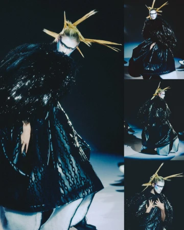 Runway fashion show featuring a model in an elaborate, dark couture gown with avant-garde styling and bold makeup against a dark background.