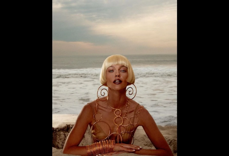 Woman on beach with blonde bob hairstyle, wearing statement jewelry. Ocean backdrop with sandy beach and sky. Beauty fashion shot.
