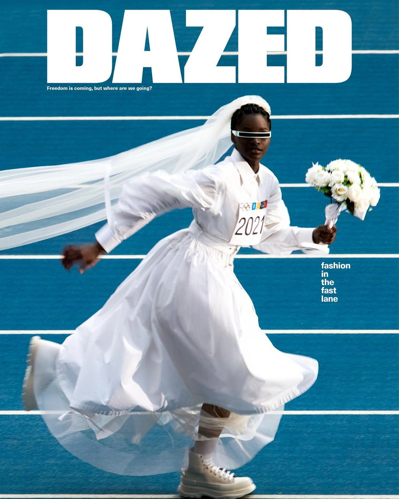 A Black woman in a white wedding dress and veil running on a blue running track while holding a bouquet of white flowers.