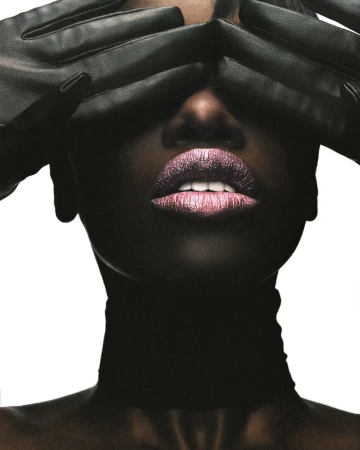 Close-up portrait of a Black woman covering her eyes with black leather gloves, wearing metallic lipstick and a black choker.