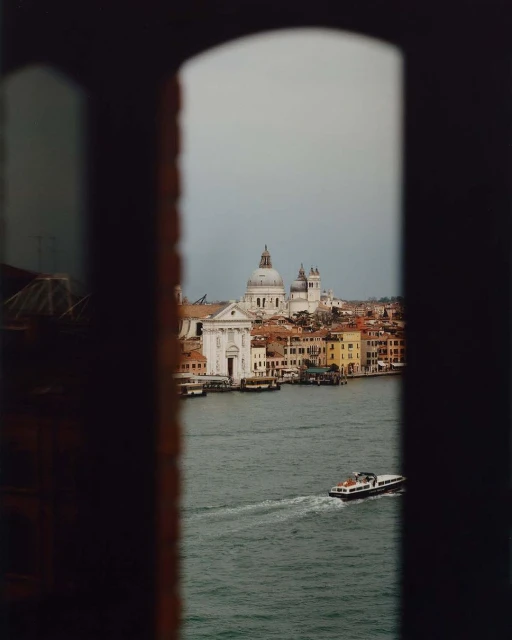 Scenic view of Venice cityscape and waterways framed by a dark window, featuring historic architecture and a boat on the water.