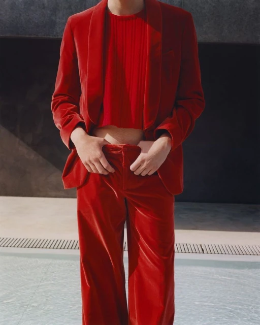 Person in a red velvet suit and top stands near a pool, creating a bold fashion statement with a blend of formal and casual styles.