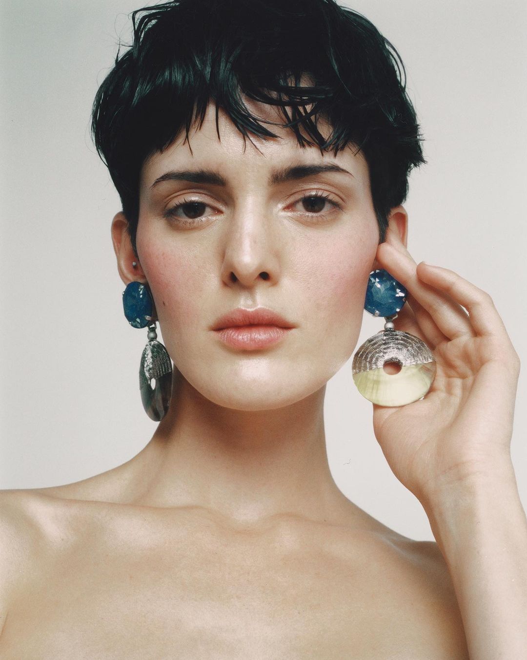 Close-up studio shot of a fair-skinned adult female model with short black hair and large, statement earrings. Beauty and fashion.