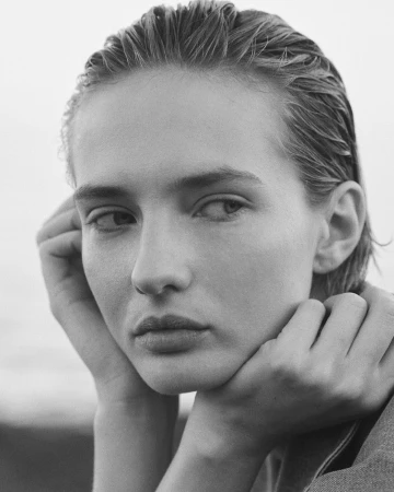 Monochrome portrait of a woman with wet-look slicked-back hair resting her chin on her hands, photographed by Carlo Piro in Paris.