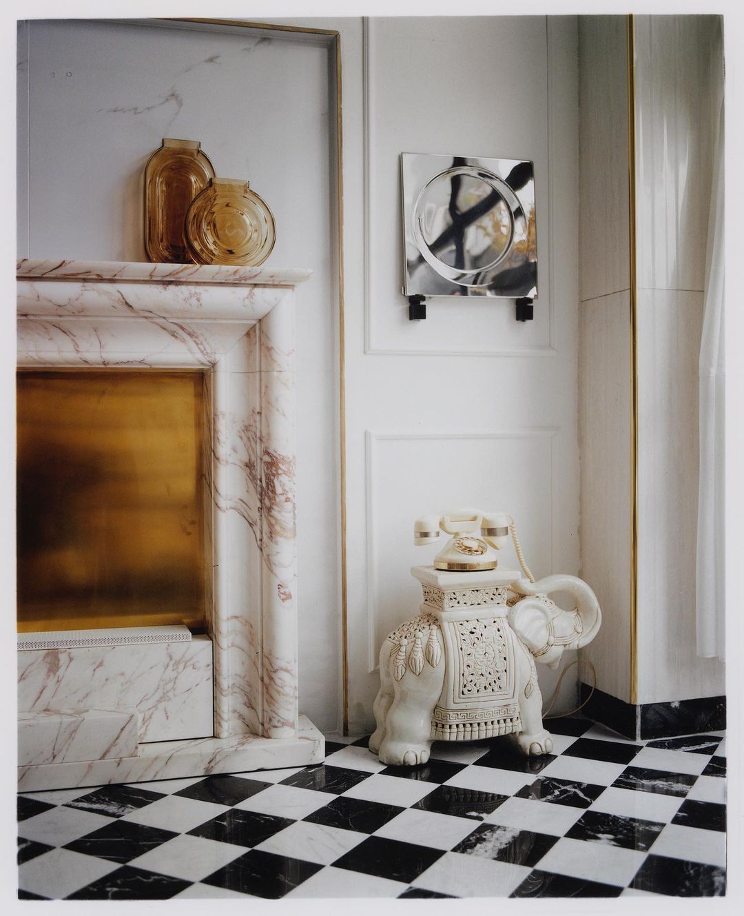 Elegant interior featuring a marble fireplace, decorative glass vases, a stylish mirror, and a vintage elephant-shaped telephone stand.