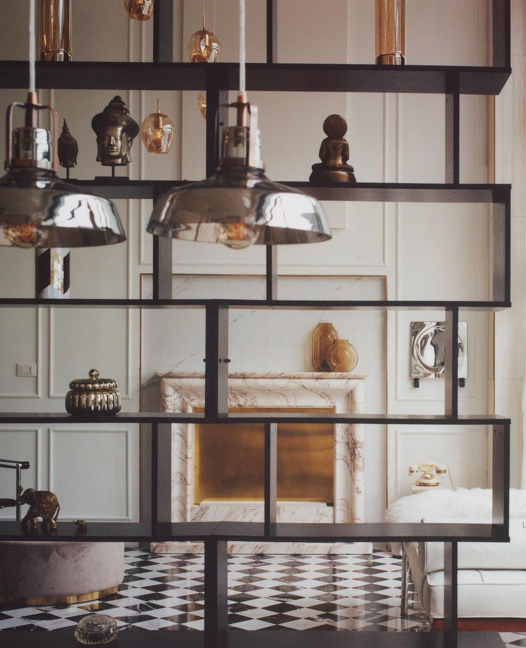 Stylish home interior with modern display shelving unit, vintage decor, marble fireplace, overhead pendant lighting, and checkered floor.