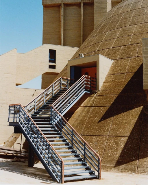 Architectural shot features concrete building with a dome, stairs, and modern design under a clear blue sky during daylight.