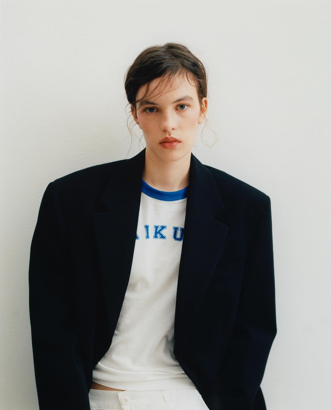 Portrait of a woman wearing an oversized black blazer over a white graphic t-shirt against a plain white background