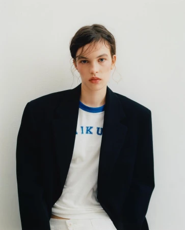 Portrait of a woman wearing an oversized black blazer over a white graphic t-shirt against a plain white background