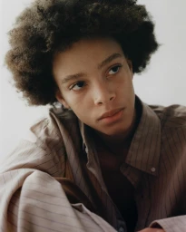 Portrait of a Black man with an afro wearing a striped shirt against a plain white background