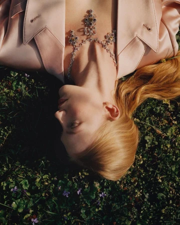 Model lying in green grass wearing a light pink jacket and ornate diamond necklace by photographer Carlo Piro