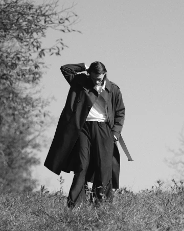 Monochrome portrait of a man in a long coat walking outdoors through a grassy field captured by Carlo Piro