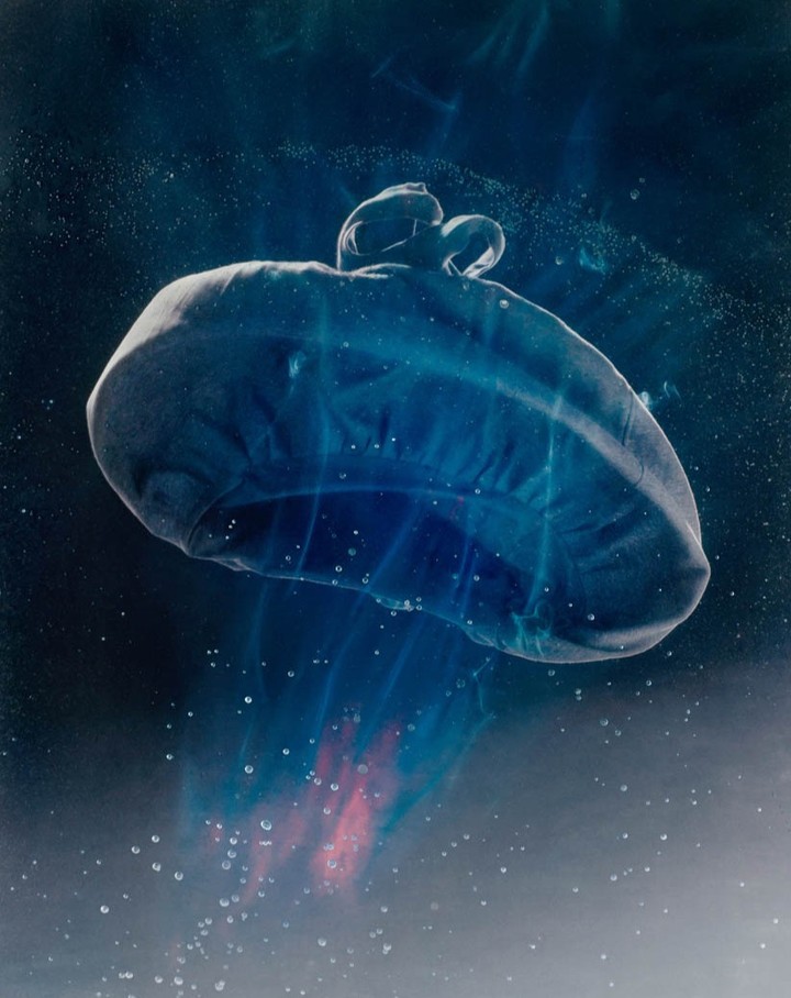 Abstract underwater still life photography showcasing a floating, translucent jellyfish-like form with flowing tendrils in a dark blue environment.
