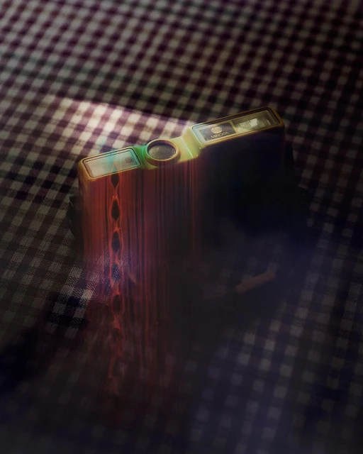 Vintage gold and green film camera resting on a checkered tablecloth in a dimly lit setting, creating a nostalgic and moody scene.