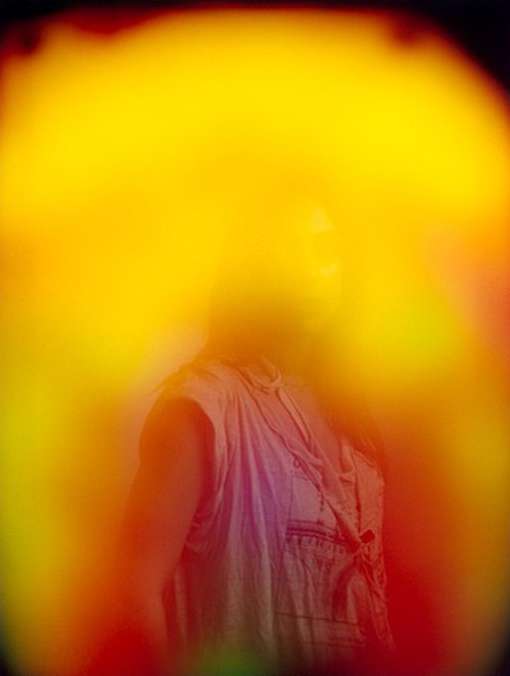 Abstract portrait of an adult wearing a light-colored shirt surrounded by a yellow and orange aura, with gradients of red and green.