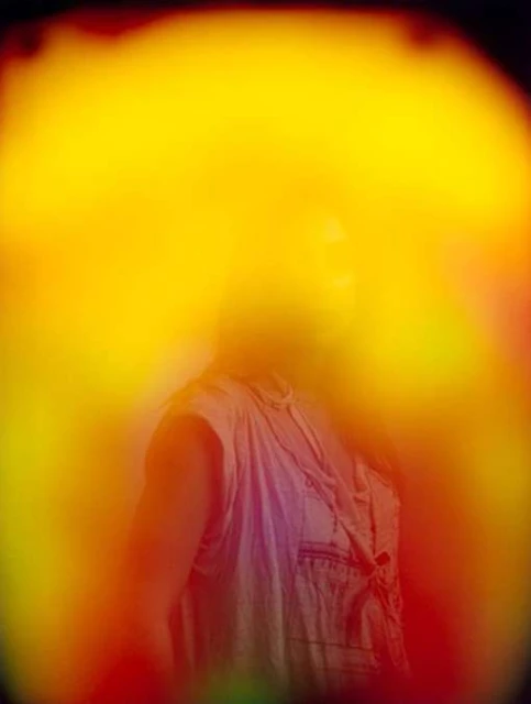 Abstract portrait of an adult wearing a light-colored shirt surrounded by a yellow and orange aura, with gradients of red and green.
