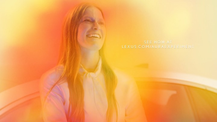 Smiling woman with light-brown hair wearing a white blouse with a tied collar, softly illuminated by an aura of orange and yellow light.