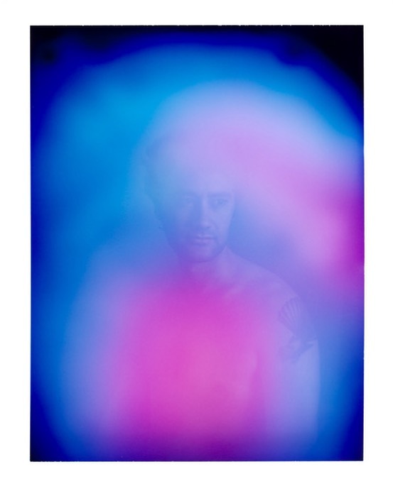 Portrait of a blurred man with pink and blue aura. Man's head and shoulders are visible; the image is heavily blurred with light.