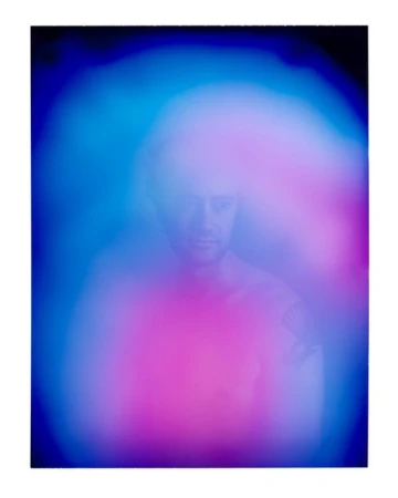 Portrait of a blurred man with pink and blue aura. Man's head and shoulders are visible; the image is heavily blurred with light.