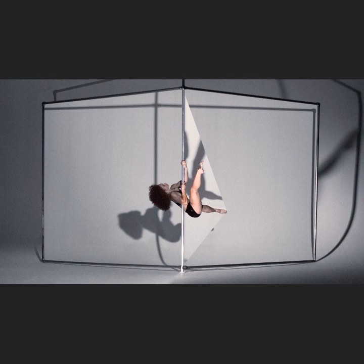 An adult female performs pole fitness in a studio with a custom square frame, showcasing strength, flexibility, and a modern aesthetic.