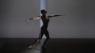 Elegant ballet dancer poses in a modern dance studio. She is wearing a dark leotard with outstretched arms in a backlit silhouette.