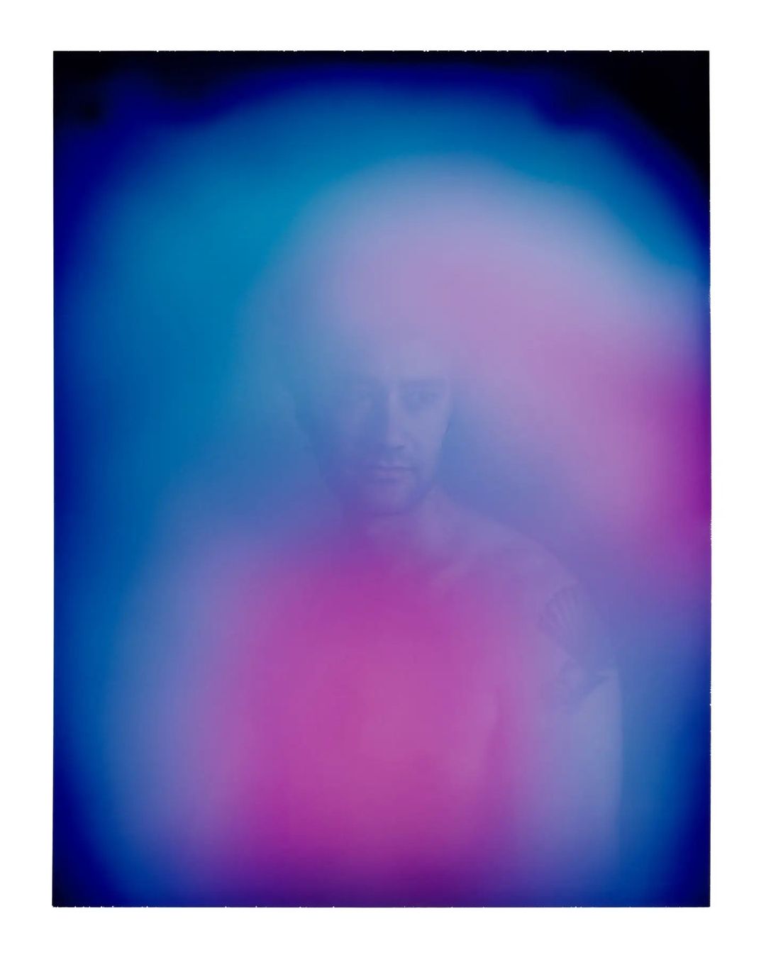 Man in a surreal portrait with glowing neon pink and blue aura. The image features blurred effects and artistic photography.