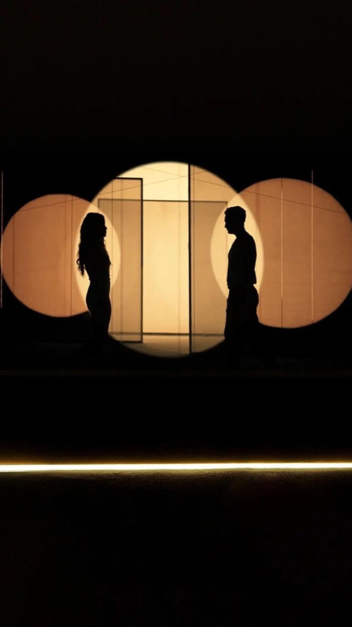 Silhouette of an adult man and woman facing each other against lit circles in a dimly lit room. Couple facing each other.