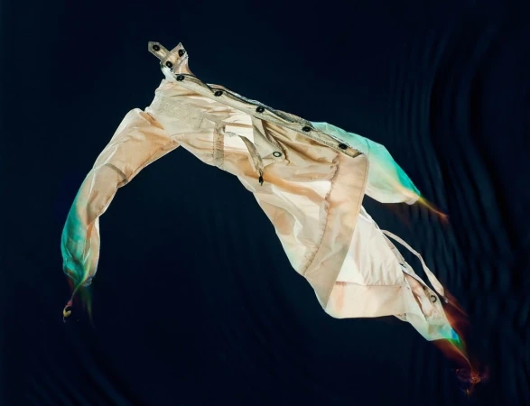 Floating beige jacket with colorful light trails against a dark textured background photographed by Carlo Van De Roer