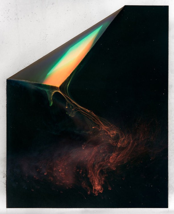 Abstract art photograph featuring a curled paper sheet with an iridescent sheen that drips into a black and red ink cloud.