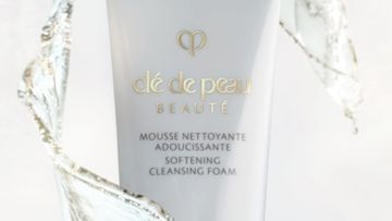 A white tube of Clé de Peau Beauté Softening Cleansing Foam, surrounded by splashing water against a white background.