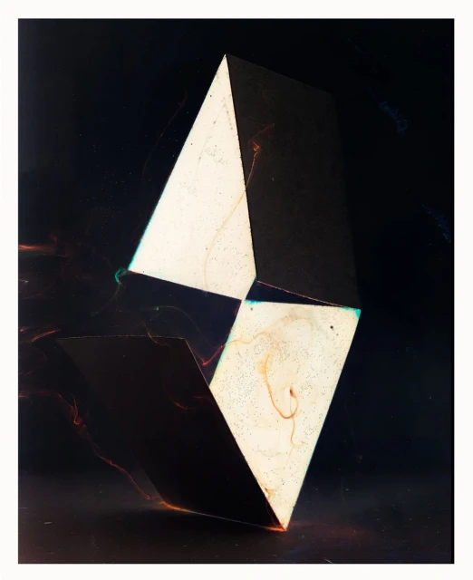Abstract geometric sculpture featuring light and shadow contrasts against a dark background, creating a visually striking composition.