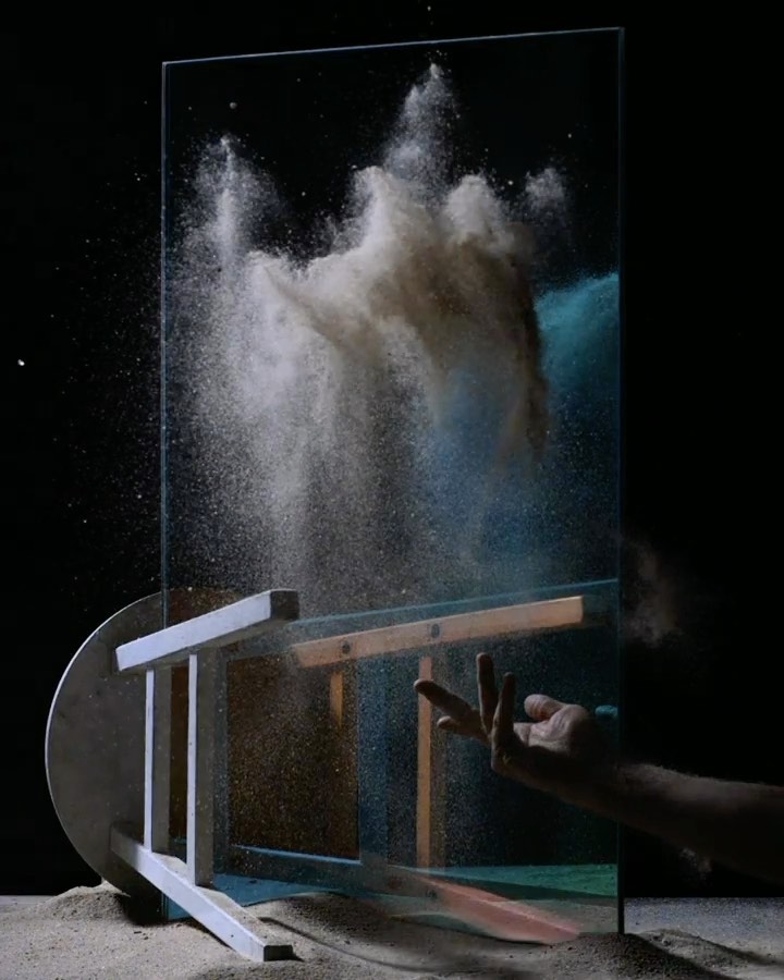 Abstract image of dust suspended in the air after being thrown at a sheet of glass, with a hand and a chair also visible.