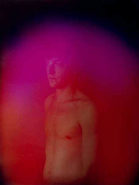 Abstract portrait of a shirtless adult male with light skin tones surrounded by pink and red aura-like colors on a dark background.