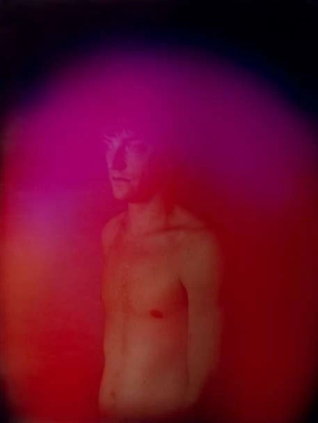 Abstract portrait of a shirtless adult male with light skin tones surrounded by pink and red aura-like colors on a dark background.
