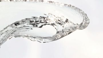 Close-up of water twisting in the air, forming a clear, translucent arc against a bright white background.