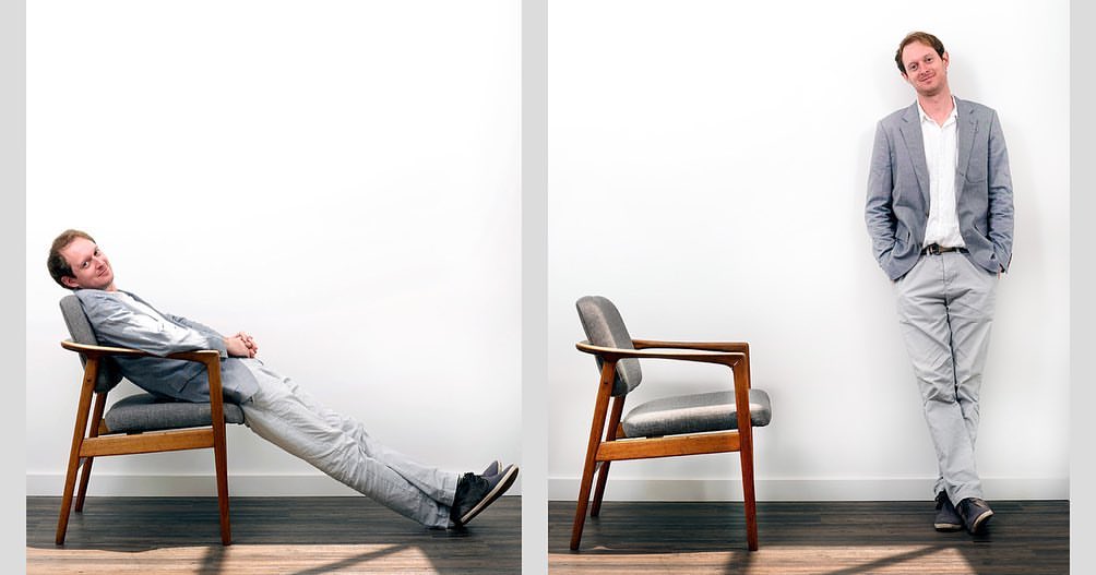 Man in grey suit poses in two compositions: reclining in a wood chair and standing against a white wall, minimalist aesthetic.