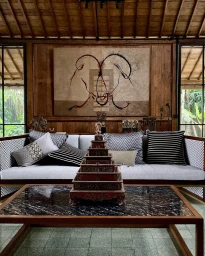 Interior living room with wooden wall panels, a grey sofa with patterned pillows, and a stacked tiered decorative box on a coffee table.