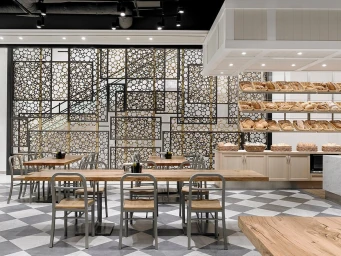 Bakery interior with wooden dining tables, metal chairs, and shelves displaying loaves of bread in wicker baskets.