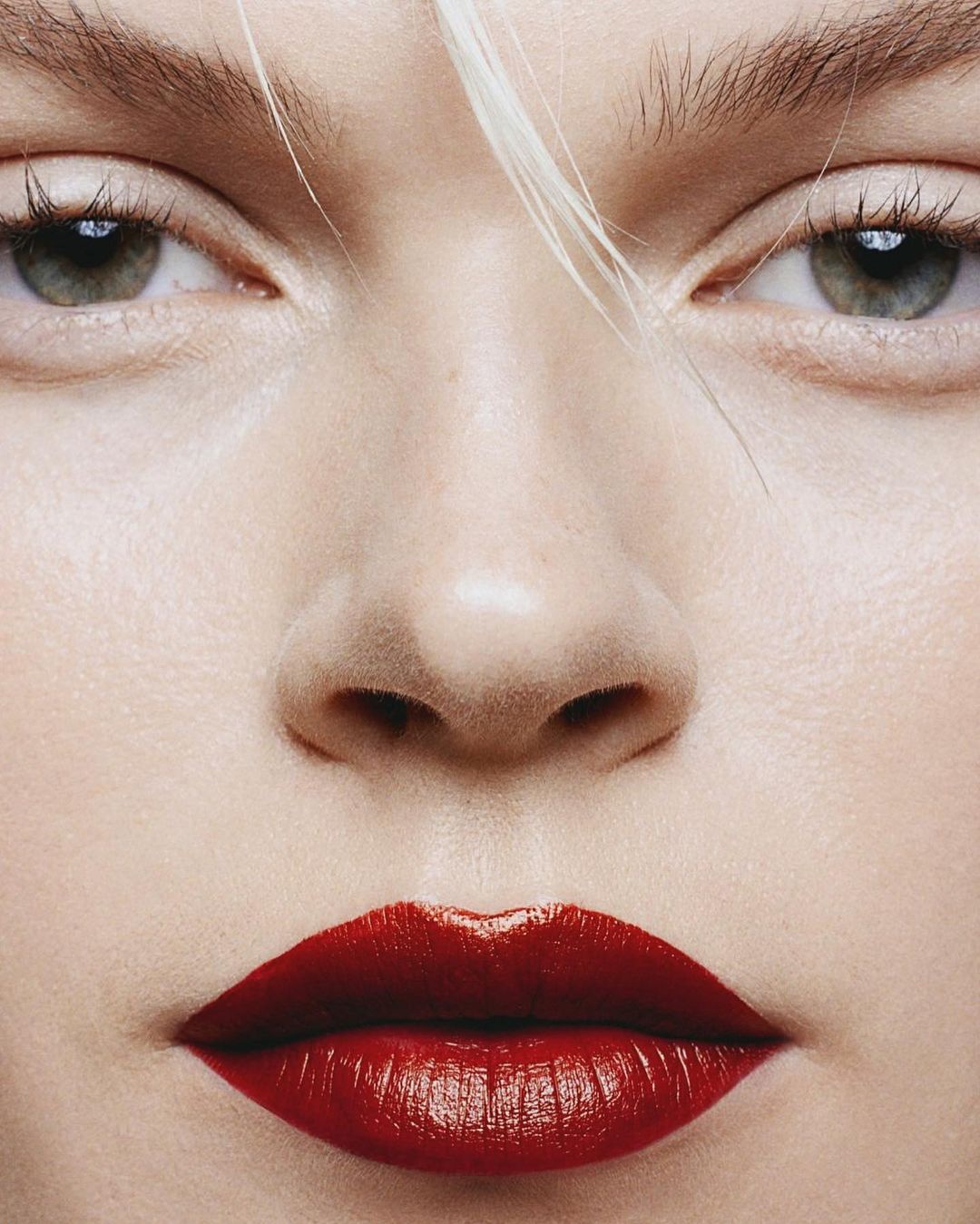 Close-up portrait of a woman's face featuring red lipstick, light skin, and green eyes, with white blonde hair visible.
