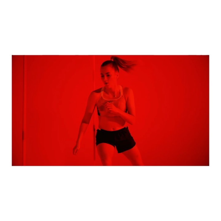 Athletic woman in sports bra and shorts exercising in a red-lit room, captured in medium shot, highlighting fitness and active lifestyle.