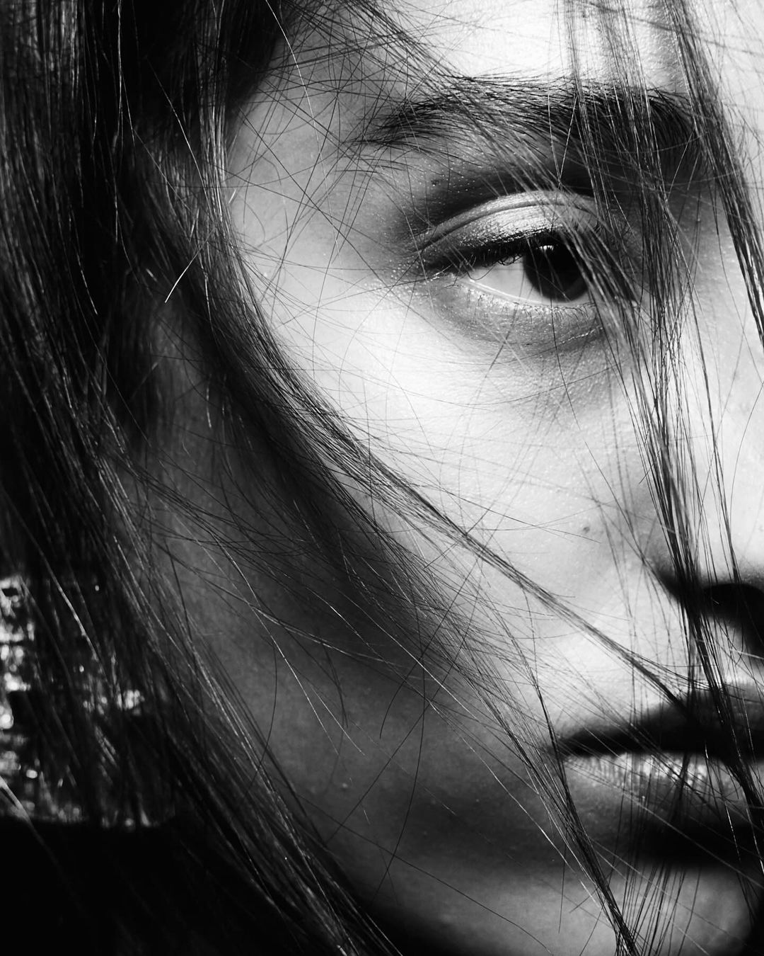 Close-up black and white portrait of a woman with strands of hair falling across her face by Carlos Garcia