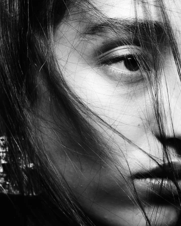 Close-up black and white portrait of a woman with strands of hair falling across her face by Carlos Garcia
