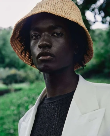 Portrait of a Black man wearing a straw bucket hat and white blazer outdoors by Carlos Garcia