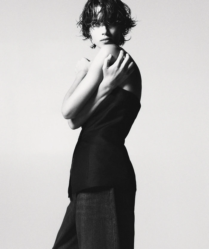 Black and white portrait of a woman with short wet hair wearing a dark strapless top against a seamless background.