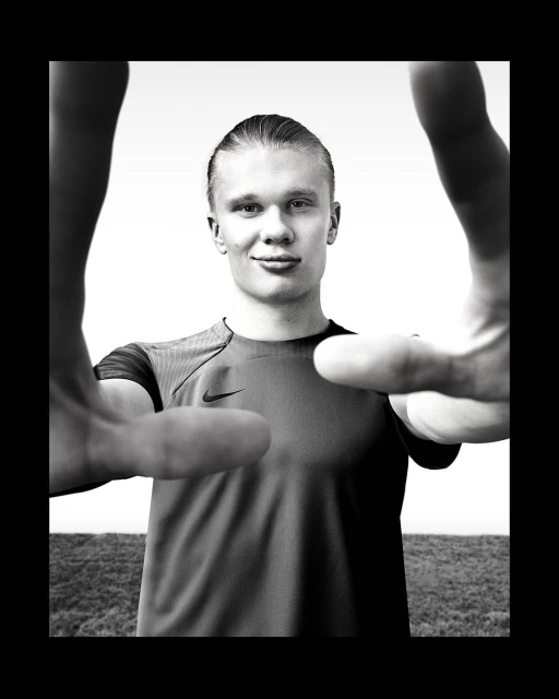 Close-up black and white portrait of a smiling athlete with slicked-back hair, framed by two hands, against a bright, blurred background.