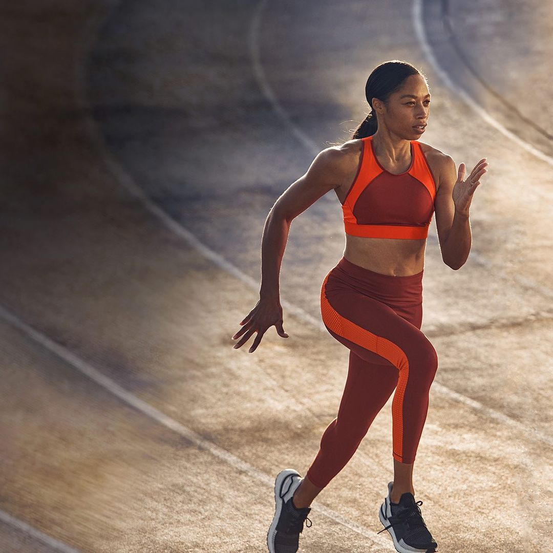 Athletic woman in sports bra and leggings running on a track. Runner sprinting with determination in activewear and running shoes.